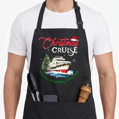 Christmas cruise memory apron - Watercolor cruise ship and Christmas tree with red and green text and Santa hat — shown on a black cotton canvas apron against a white background