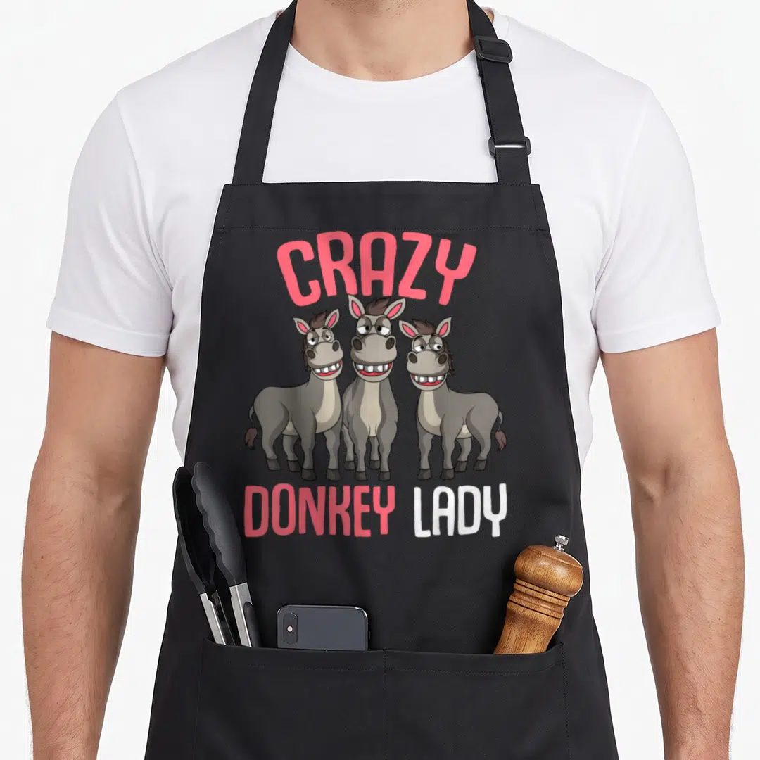 Donkey owner funny apron - Three cartoon donkeys with pink CRAZY DONKEY LADY text — shown on a black cotton canvas apron against a white background