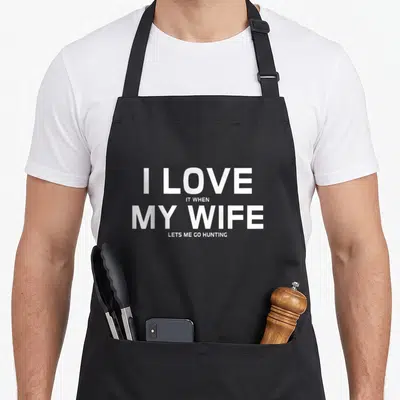 Hunting wife apron - White stacked text reading I LOVE IT WHEN MY WIFE LETS ME GO HUNTING — shown on a black cotton canvas apron against a white background