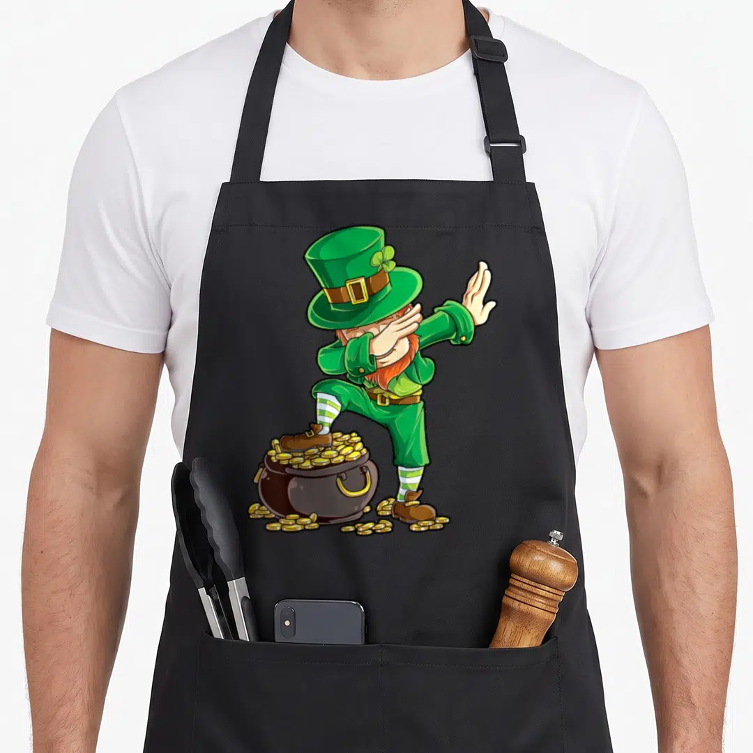Leprechaun st patrick day aprons - Cartoon leprechaun dabbing on overflowing gold pot wearing green hat and striped — shown on a black cotton canvas apron against a white background