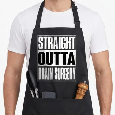 Straight hospital apron - Stacked distressed typography reading STRAIGHT OUTTA BRAIN SURGERY in white and black within — shown on a black cotton canvas apron against a white background