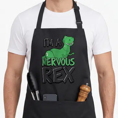 Nervous dog breed aprons - Green cartoon T-Rex with text I'm A Nervous Rex on black background — shown on a black cotton canvas apron against a white background