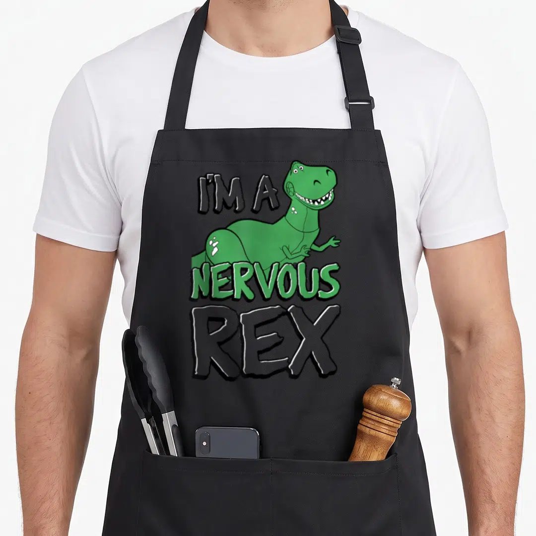 Nervous dog breed aprons - Green cartoon T-Rex with text I'm A Nervous Rex on black background — shown on a black cotton canvas apron against a white background