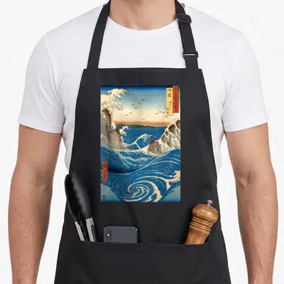 Navaro japanese apron - Blue and white swirling ocean waves with orange sky and kanji text boxes in retro Japanese art — shown on a black cotton canvas apron against a white background