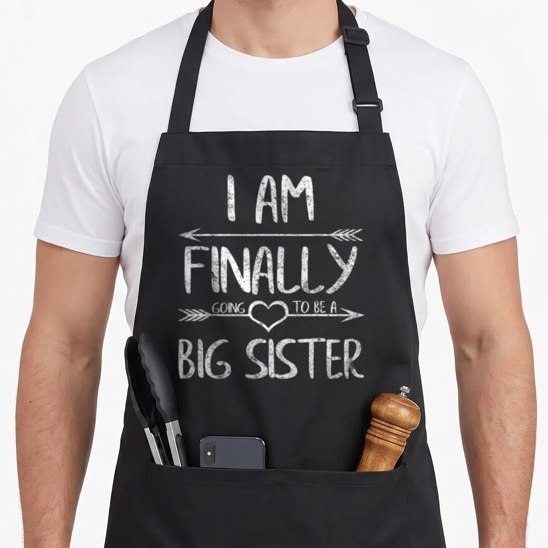 Older sister finally apron - White distressed text reading I AM FINALLY GOING TO BE A BIG SISTER with arrows and heart — shown on a black cotton canvas apron against a white background