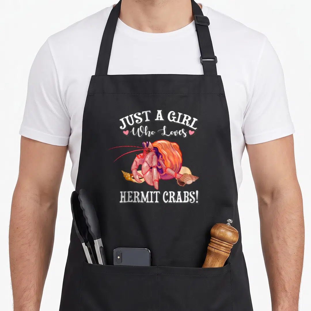 Pet crab apron - Cartoon hermit crab with seashells and text Just A Girl Who Loves Hermit Crabs — shown on a black cotton canvas apron against a white background
