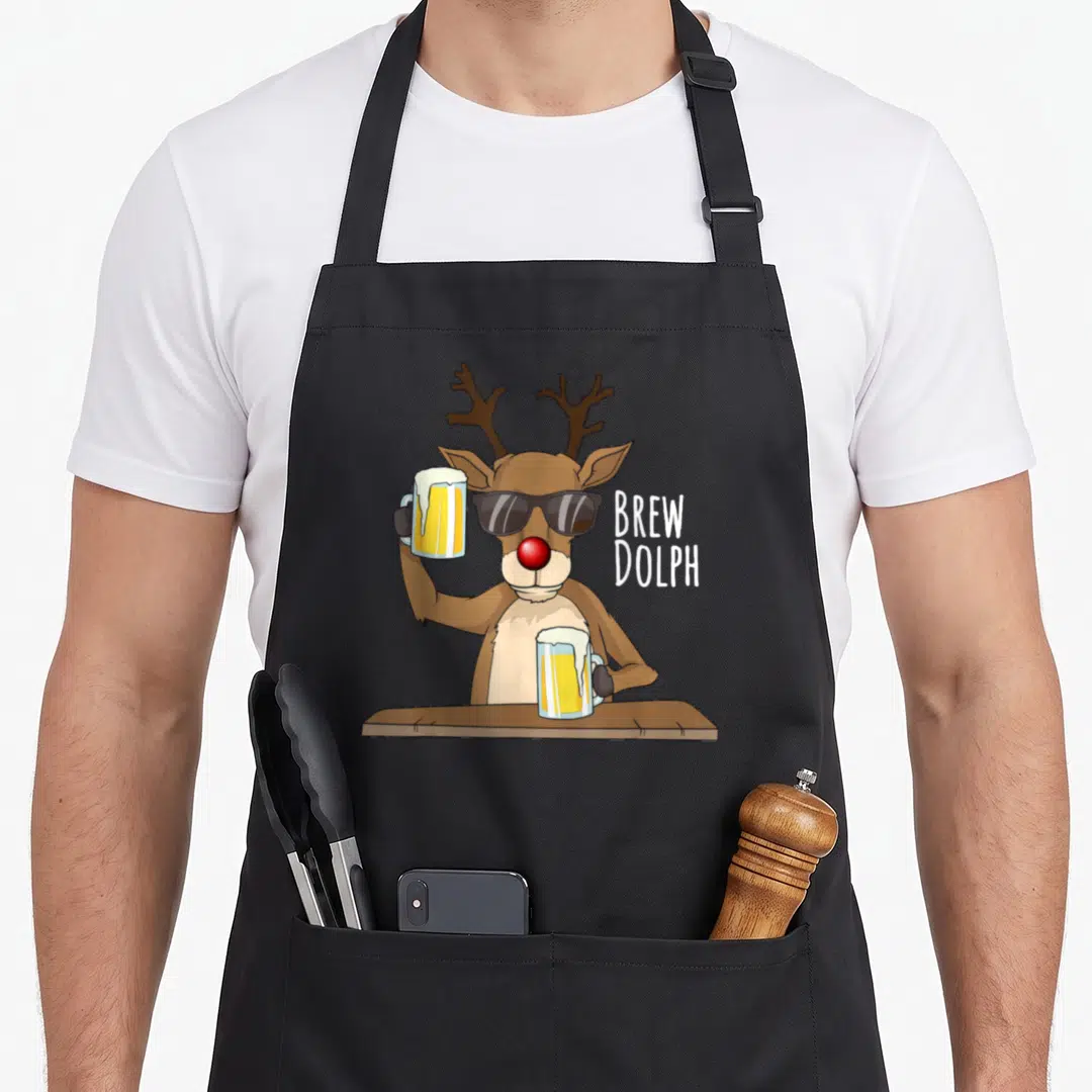 Alcohol christmas apron - Cartoon brown reindeer in sunglasses holding two yellow beer mugs with white text BREW DOLPH — shown on a black cotton canvas apron against a white background