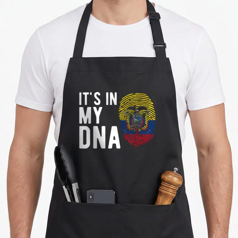 Dna ecuador apron - IT'S IN MY DNA text beside fingerprint with coat of arms in yellow blue red white — shown on a black cotton canvas apron against a white background