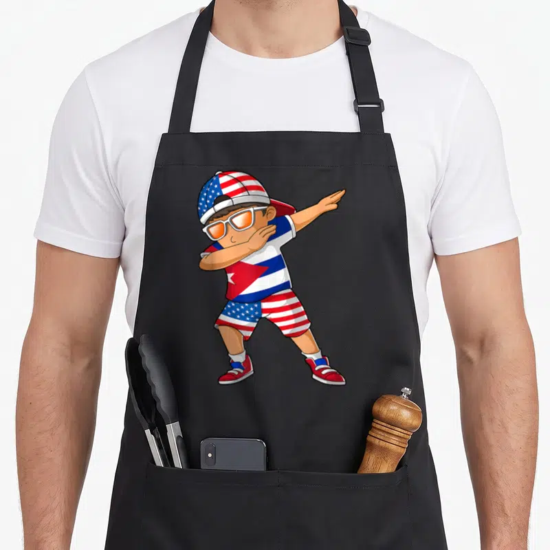 Cuba patriotic american flag apron - Cartoon boy dabbing wearing clothes patterned with American and Cuban flags in red — shown on a black cotton canvas apron against a white background