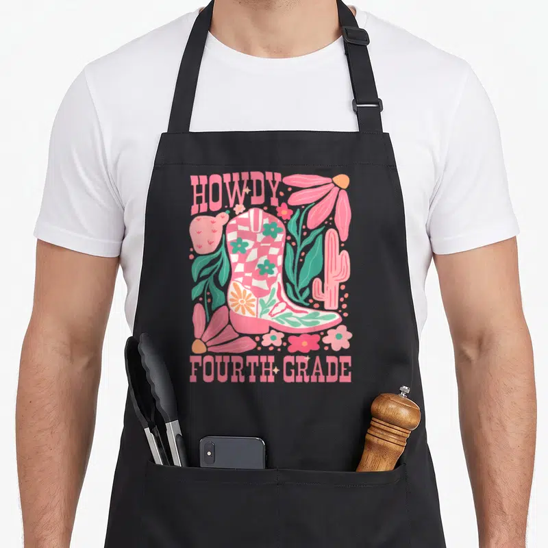 Howdy teacher apron - Pink cowboy boot with checkered pattern surrounded by cacti and flowers with HOWDY FOURTH GRADE — shown on a black cotton canvas apron against a white background