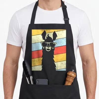 80s alpaca apron - Grey llama silhouette with sunglasses on diagonal yellow cream blue red stripes — shown on a black cotton canvas apron against a white background