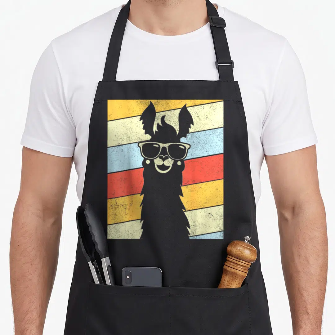 80s alpaca apron - Grey llama silhouette with sunglasses on diagonal yellow cream blue red stripes — shown on a black cotton canvas apron against a white background