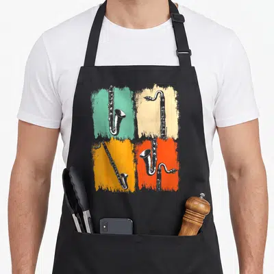 Marching clarinet life apron - Four saxophones on teal beige orange and red retro brush strokes — shown on a black cotton canvas apron against a white background