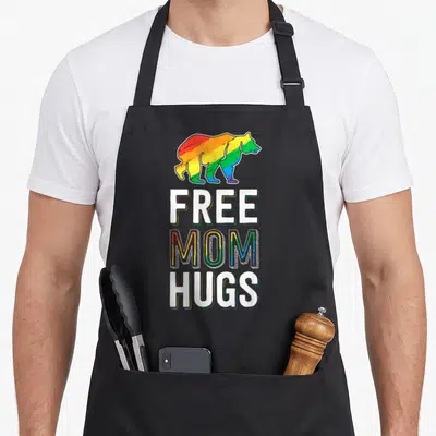 Lgbtq pride apron - Rainbow bear above white and striped MOM HUGS text in cartoon style — shown on a black cotton canvas apron against a white background