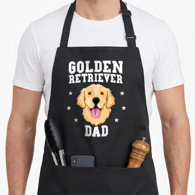 Father dog golden retriever apron - Cartoon golden retriever head with white stars and text GOLDEN RETRIEVER DAD — shown on a black cotton canvas apron against a white background