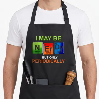Natural laboratory apron - Periodic table tiles N, Er, Dy with text I MAY BE N ER DY BUT ONLY PERIODICALLY — shown on a black cotton canvas apron against a white background