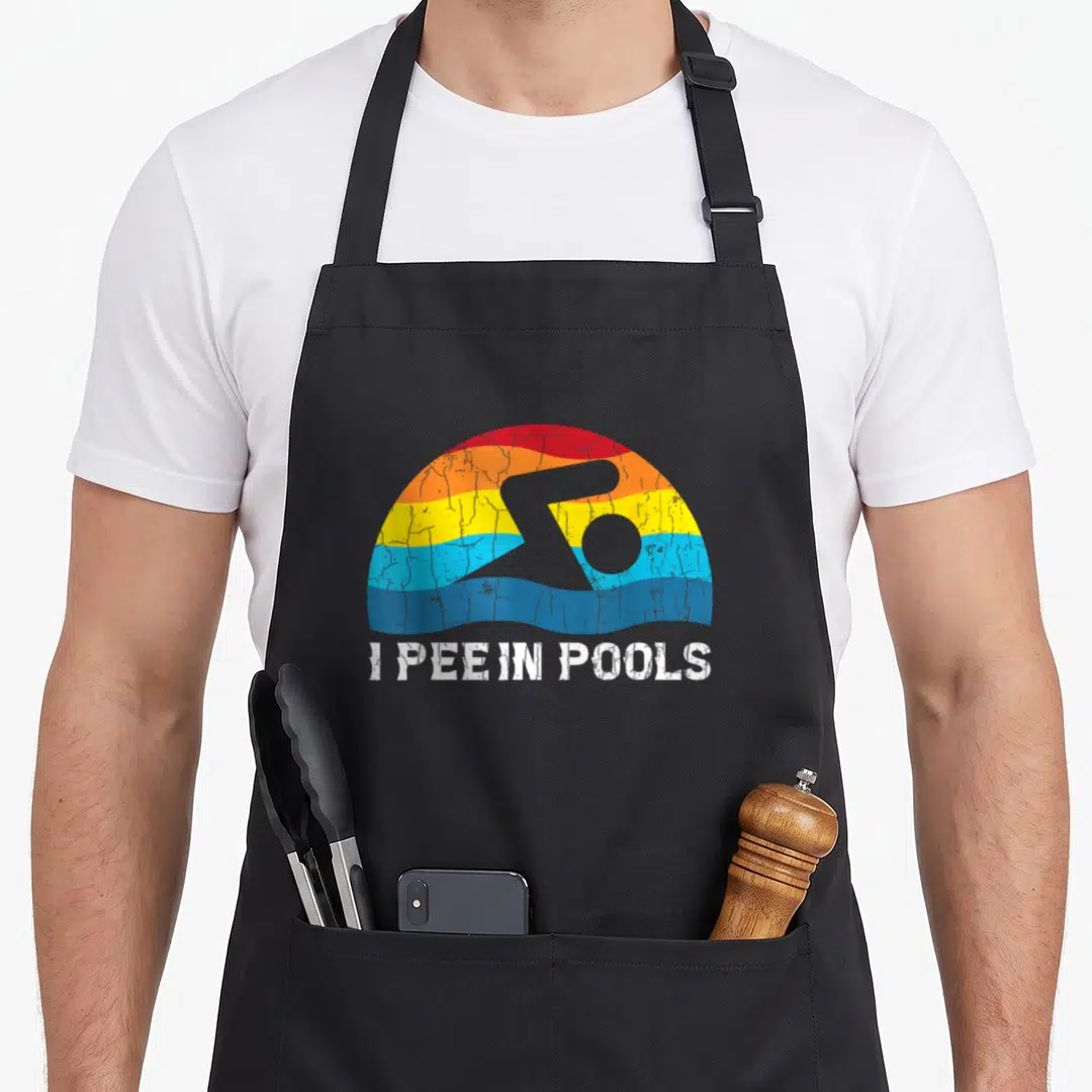 Pee i love swimming apron - I PEE IN POOLS text below grey swimmer silhouette and distressed rainbow arc — shown on a black cotton canvas apron against a white background