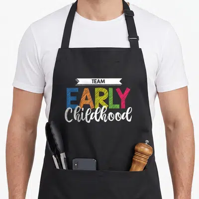 Early teacher apron - Stacked text reading TEAM EARLY Childhood in blue orange yellow green pink and white typography — shown on a black cotton canvas apron against a white background
