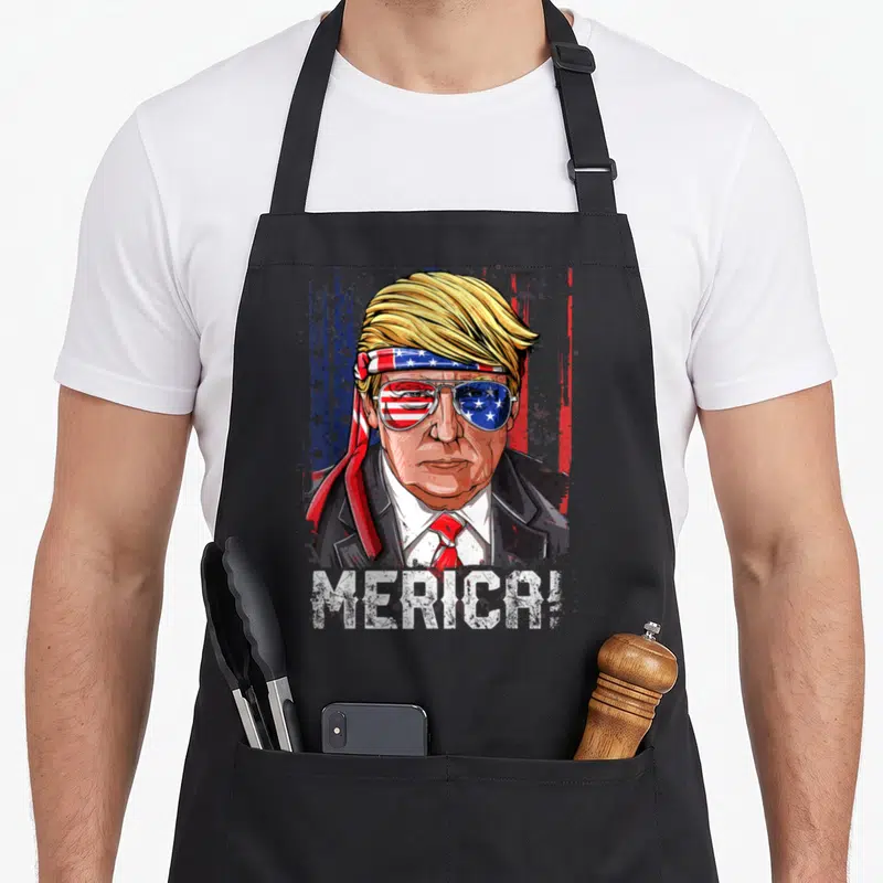 Trump 4th of july apron - Cartoon Trump portrait with flag headband sunglasses and MERICA! text on black apron — shown on a black cotton canvas apron against a white background