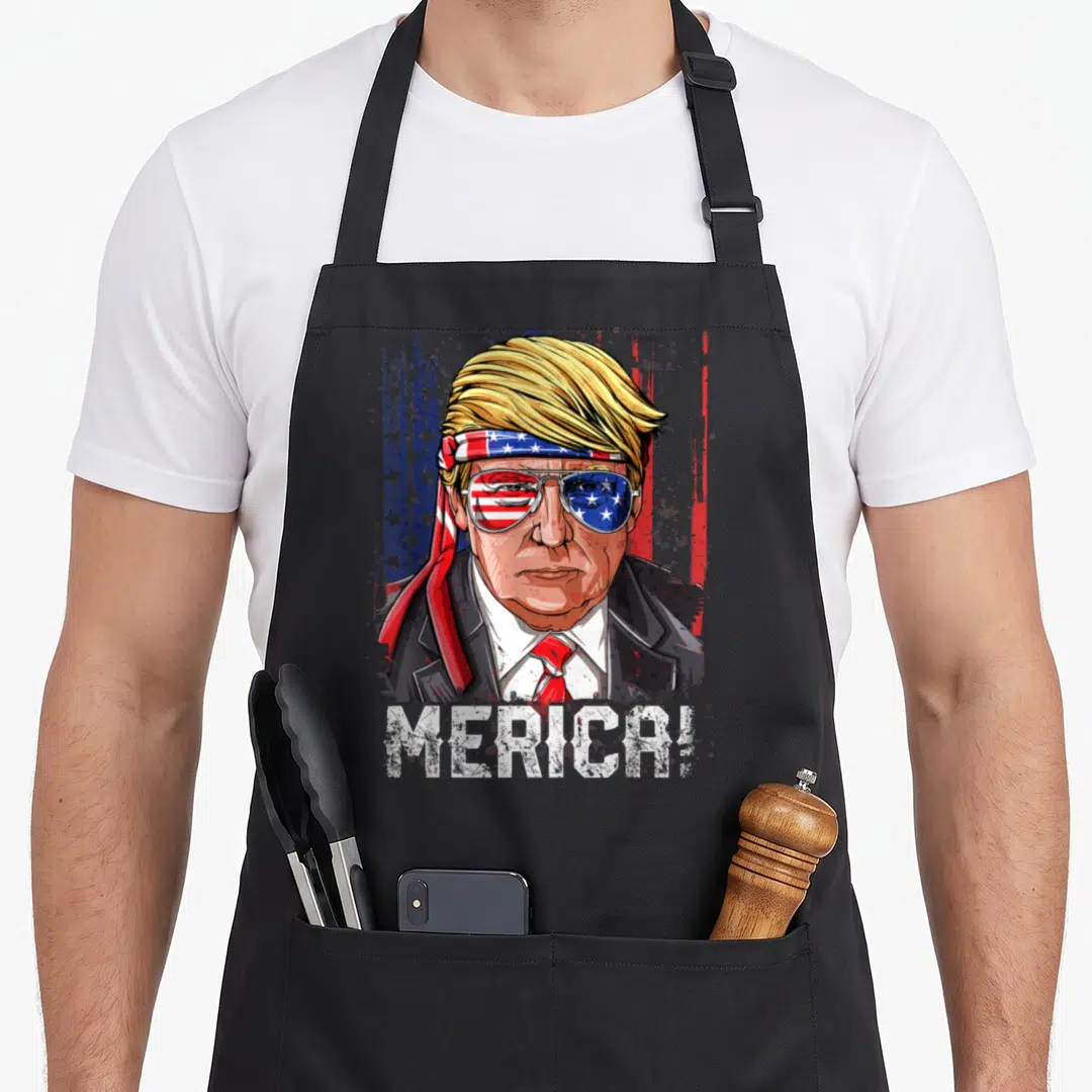 Trump 4th of july apron - Cartoon Trump portrait with flag headband sunglasses and MERICA! text on black apron — shown on a black cotton canvas apron against a white background