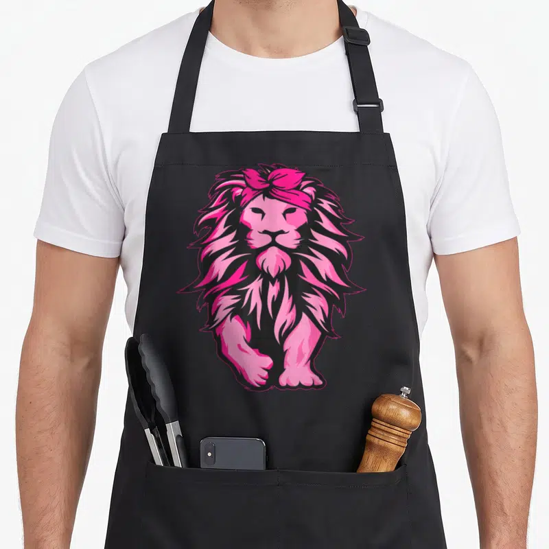 Lion breast cancer awareness aprons - Cartoon lion in pink and black wearing a pink headband — shown on a black cotton canvas apron against a white background