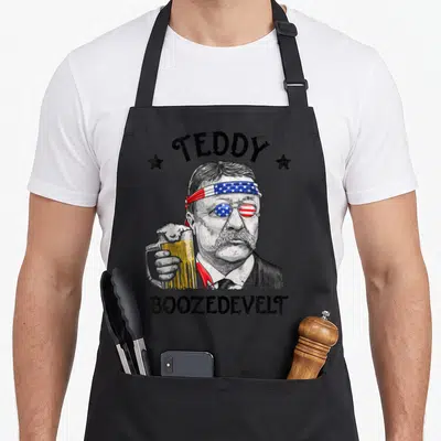Teddy 4th of july apron - Teddy Boozedevelt Roosevelt portrait with American flag headband, monocle, and beer mug — shown on a black cotton canvas apron against a white background
