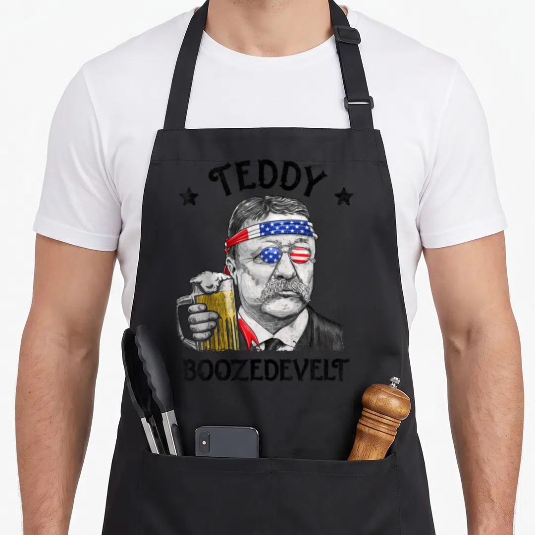 Teddy 4th of july apron - Teddy Boozedevelt Roosevelt portrait with American flag headband, monocle, and beer mug — shown on a black cotton canvas apron against a white background