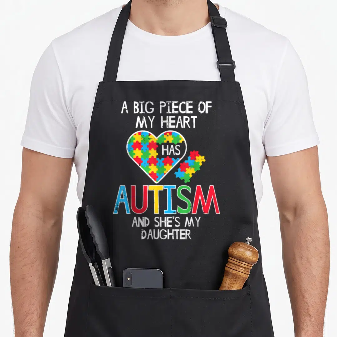 Awareness mom daughter apron - Distressed heart with multicolor puzzle pieces and text about autism and daughter — shown on a black cotton canvas apron against a white background