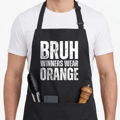 Week game aprons - White stacked text reading BRUH WINNERS WEAR ORANGE on grey background — shown on a black cotton canvas apron against a white background