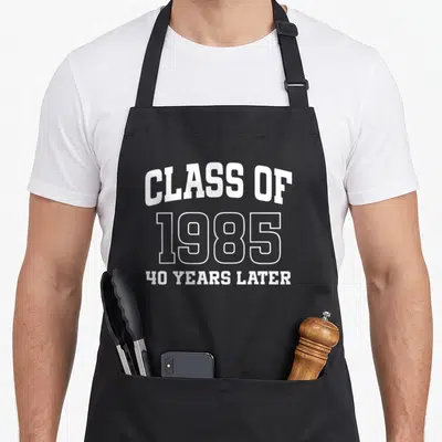 Class alumni apron - White stacked text reading Class of 1985 40 Years Later on dark background — shown on a black cotton canvas apron against a white background