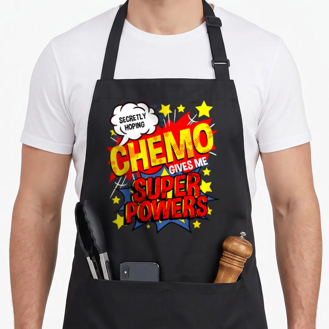 Secretly cancer man apron - Comic burst design reading Secretly Hoping Chemo Gives Me Super Powers — shown on a black cotton canvas apron against a white background