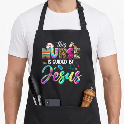 Guided nurse apron - Stacked text this NURSE IS GUIDED BY Jesus with tie-dye, leopard, and striped patterned letters — shown on a black cotton canvas apron against a white background