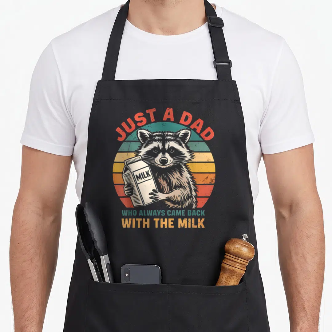 Alway came raccoon milk aprons - Raccoon holding milk carton in front of red yellow and teal striped sunset circle — shown on a black cotton canvas apron against a white background