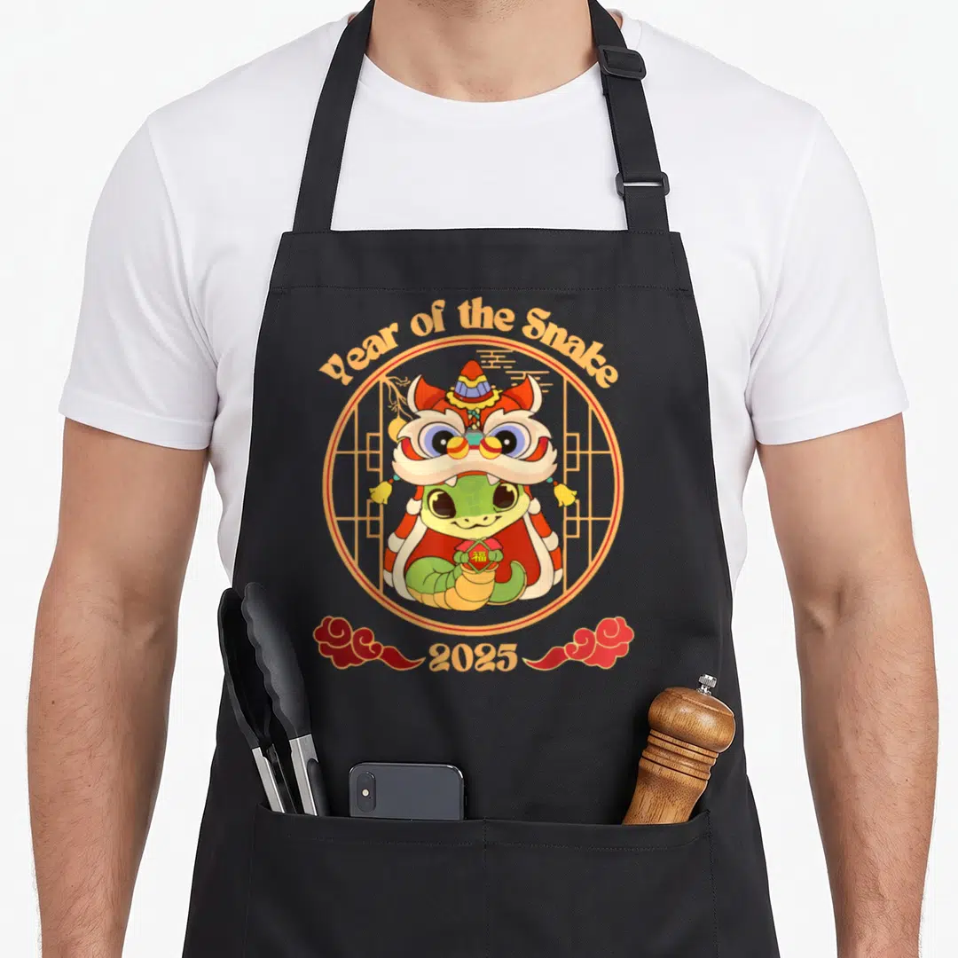 Lunar year of the snake apron - Cartoon snake in lion dance costume inside circle with 'Year of the Snake 2025' text — shown on a black cotton canvas apron against a white background