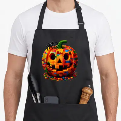 Halloween grill master apron - Colorful brick pumpkin with black spider and loose building blocks scattered at base — shown on a black cotton canvas apron against a white background