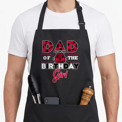 Theme ladybug apron - DAD OF THE BIRTHDAY Girl text with a red and black spotted ladybug illustration — shown on a black cotton canvas apron against a white background