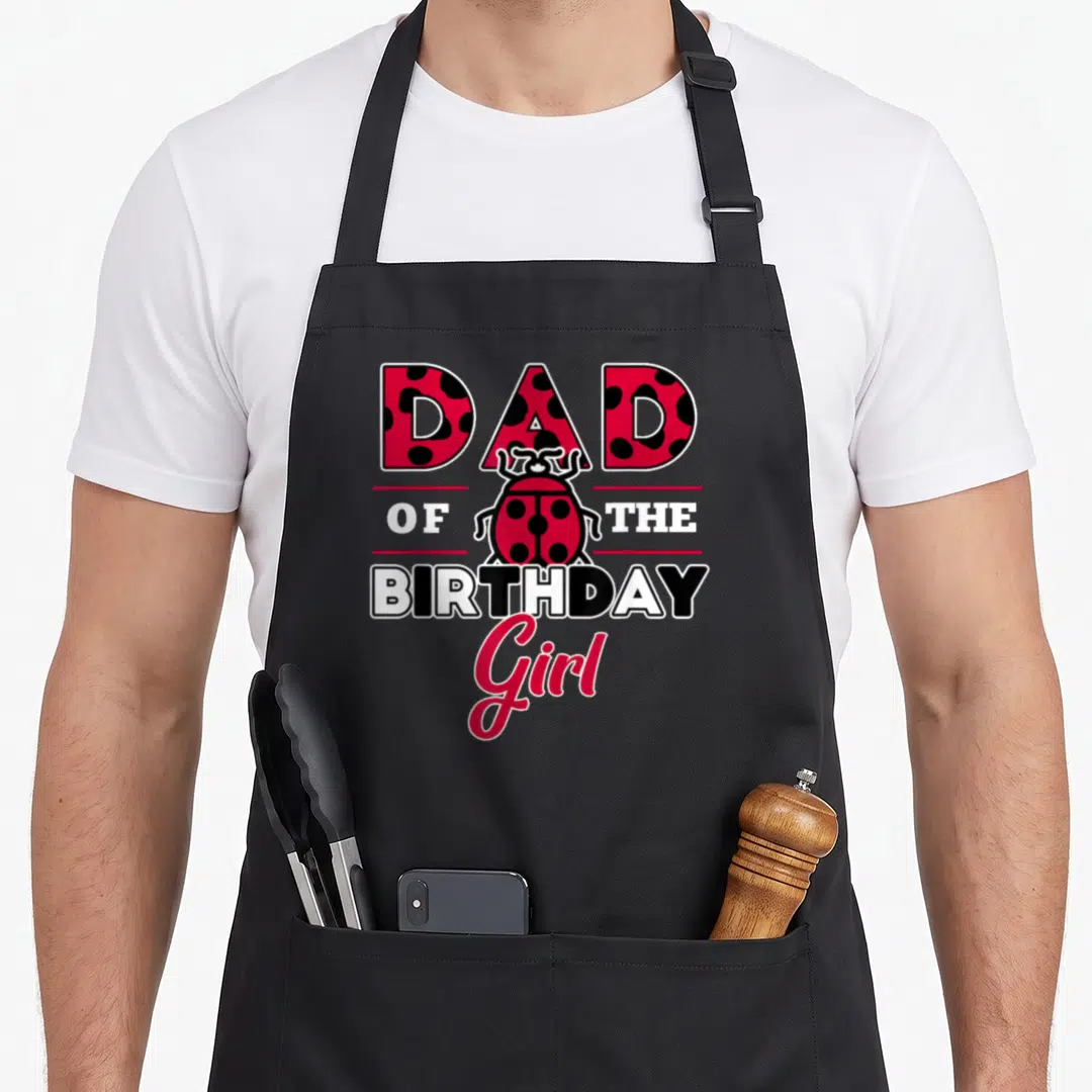 Theme ladybug apron - DAD OF THE BIRTHDAY Girl text with a red and black spotted ladybug illustration — shown on a black cotton canvas apron against a white background