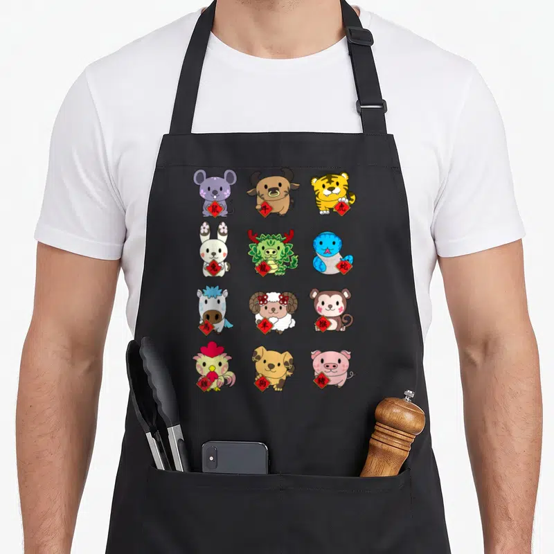 Zodiac animal apron - Twelve cartoon zodiac animals holding red diamond labels with Chinese characters in a grid layout — shown on a black cotton canvas apron against a white background