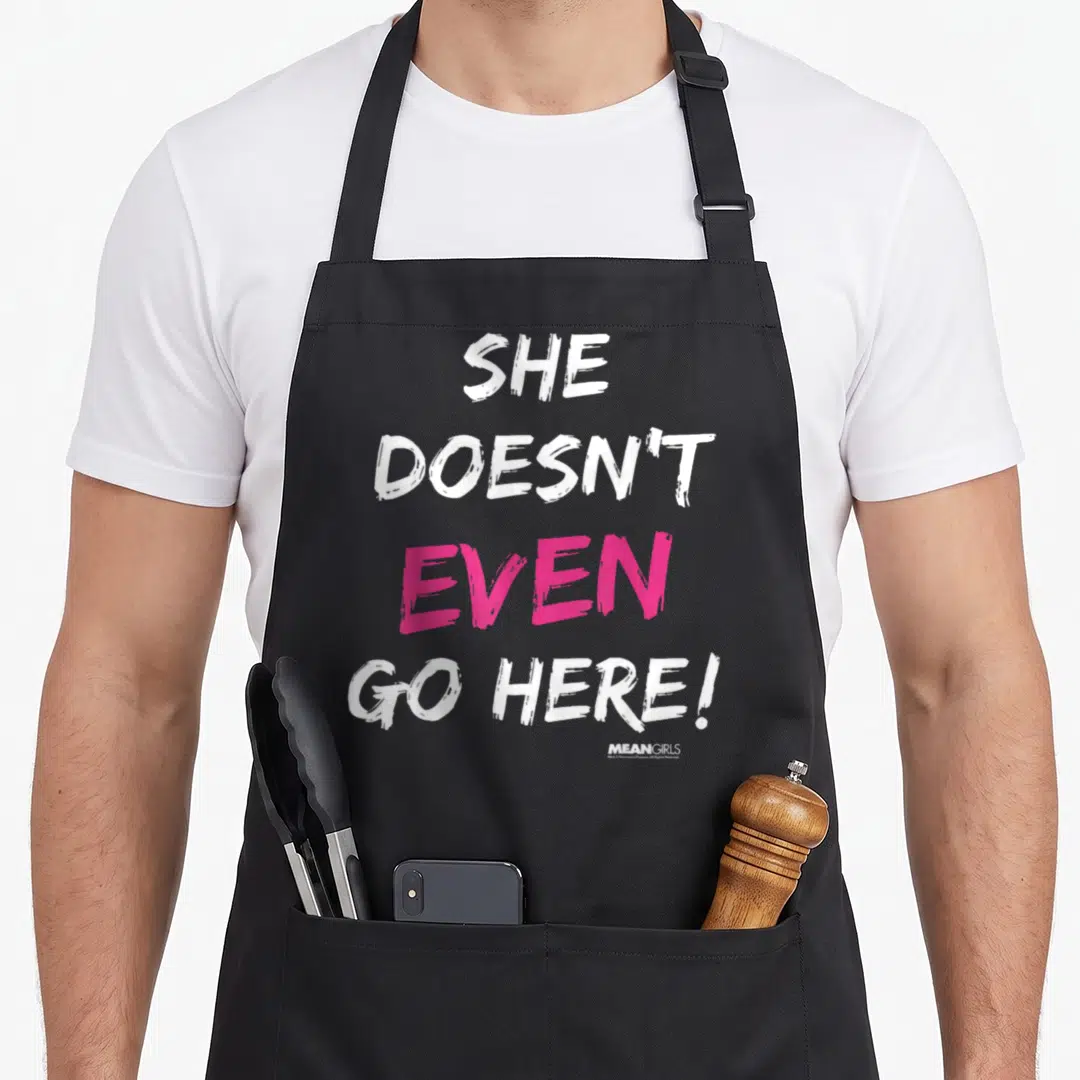Mean she doesnt apron - Stacked white and pink text reading She Doesn't Even Go Here! — shown on a black cotton canvas apron against a white background