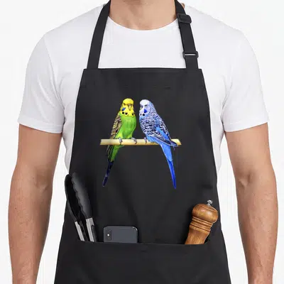 Parrot colorful aprons - Two realistic budgies perched on wood in blue, green, yellow, and tan feathers — shown on a black cotton canvas apron against a white background