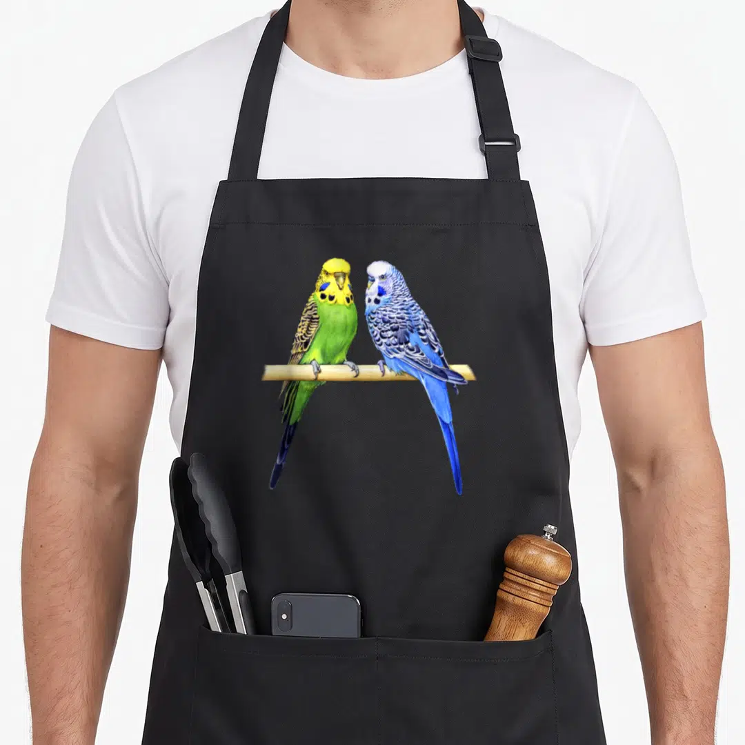 Parrot colorful aprons - Two realistic budgies perched on wood in blue, green, yellow, and tan feathers — shown on a black cotton canvas apron against a white background