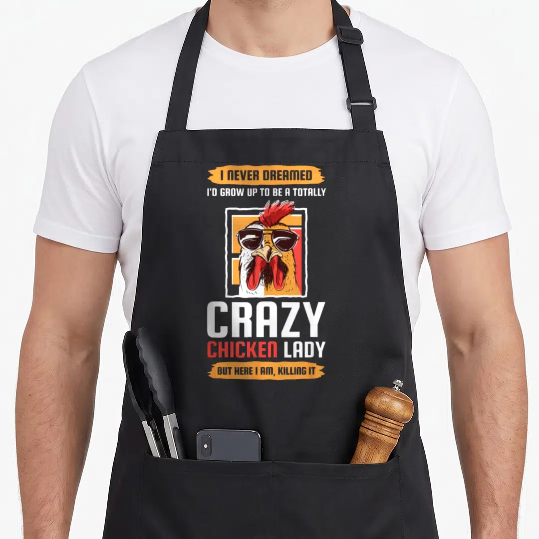 Totally chicken apron - Cartoon rooster in sunglasses on orange and white background with humorous text about being — shown on a black cotton canvas apron against a white background