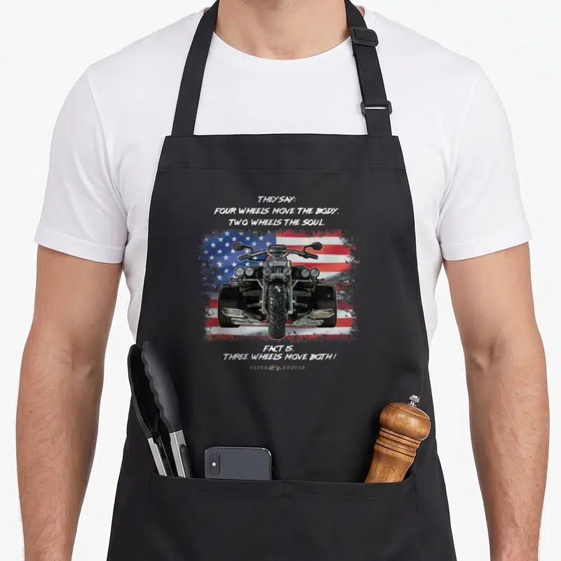 Three wheel apron - Realistic trike on distressed US flag with quote about three wheels moving both body and soul — shown on a black cotton canvas apron against a white background