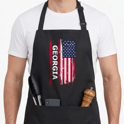 Funny georgia apron - Vertical GEORGIA text over distressed red white blue flag — shown on a black cotton canvas apron against a white background