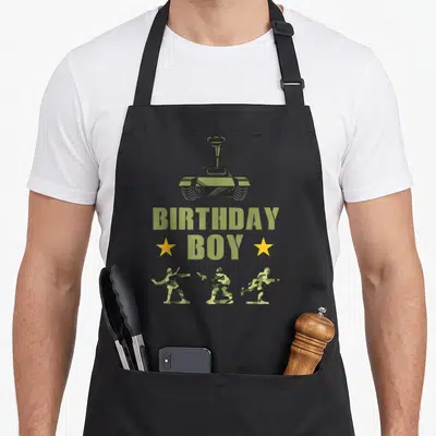 Army birthday apron - Tank above BIRTHDAY BOY text with three camo soldiers in action poses below — shown on a black cotton canvas apron against a white background