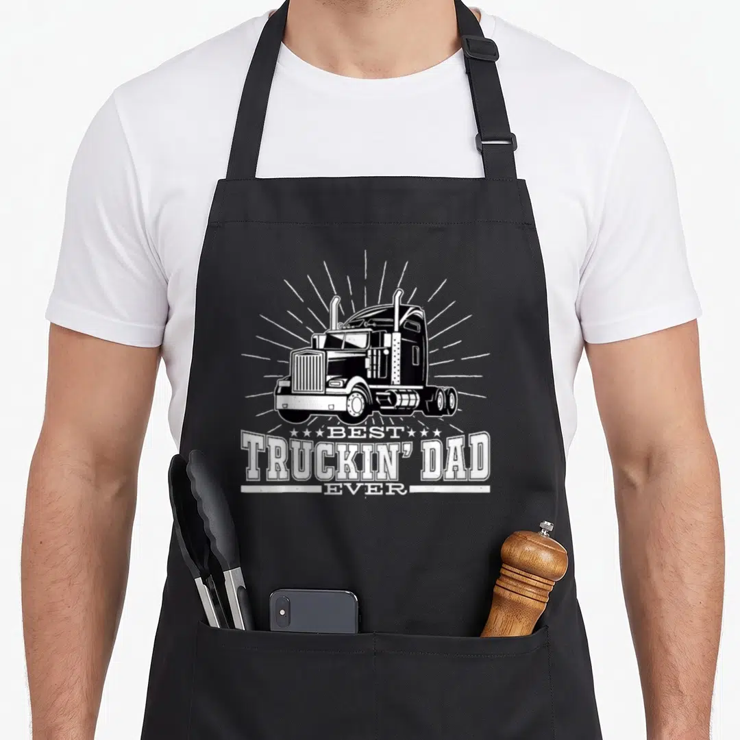 Truckin trucking truck apron - White semi-truck illustration above stacked best truckin dad ever text on black — shown on a black cotton canvas apron against a white background