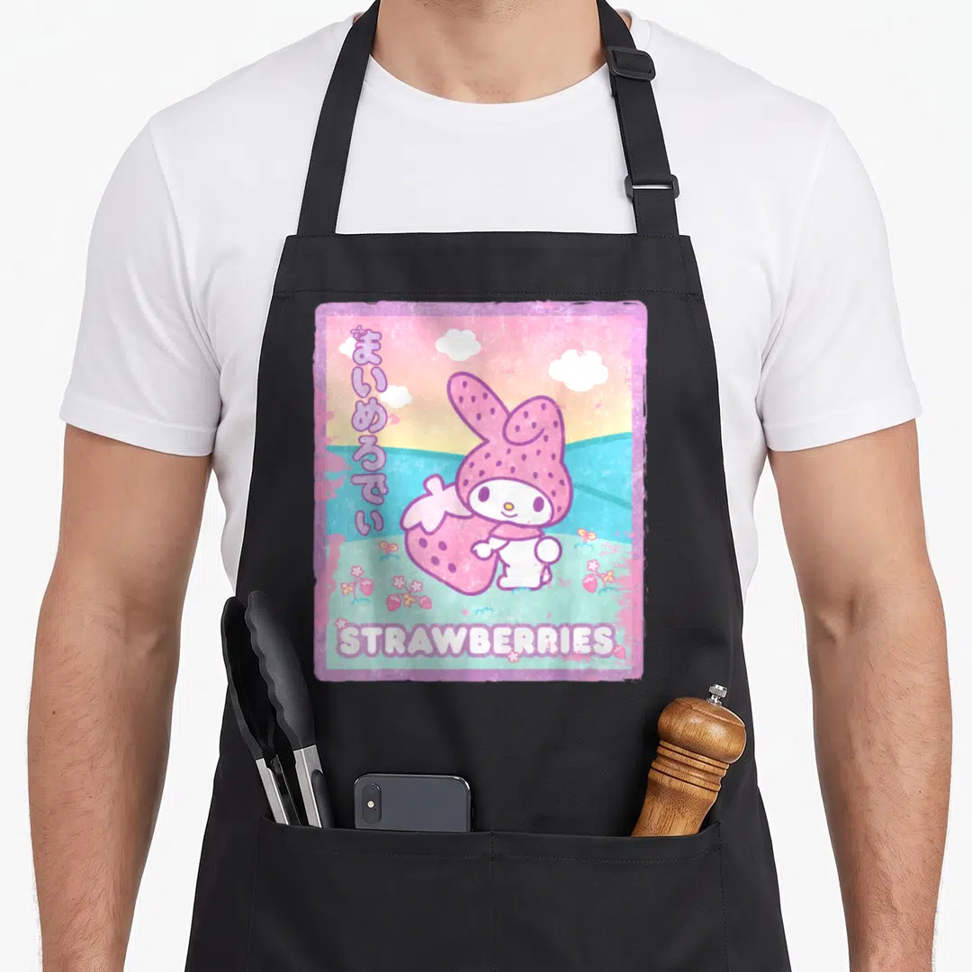 Melody milk aprons - Cartoon bunny in strawberry hood holding fruit with Japanese text and STRAWBERRIES label — shown on a black cotton canvas apron against a white background