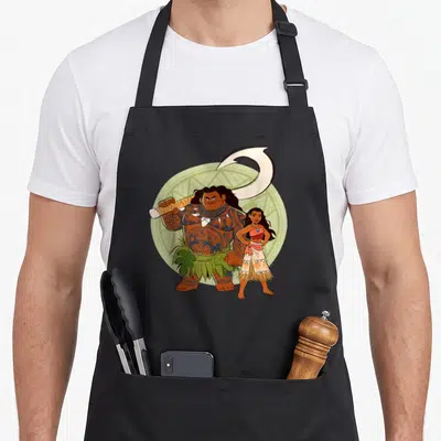 Maui friends apron - Cartoon Maui holding fishhook and Moana standing in front of green circle — shown on a black cotton canvas apron against a white background