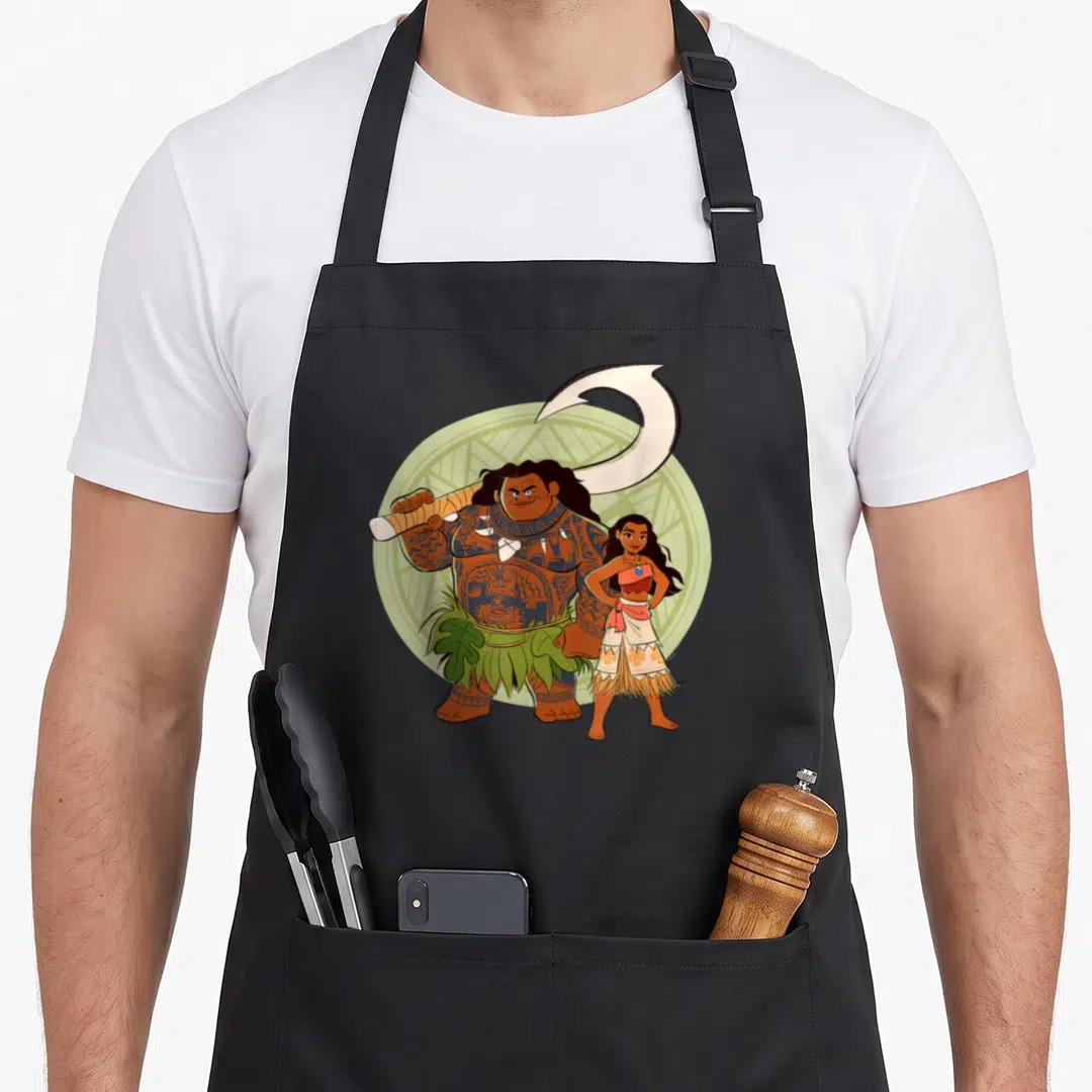 Maui friends apron - Cartoon Maui holding fishhook and Moana standing in front of green circle — shown on a black cotton canvas apron against a white background