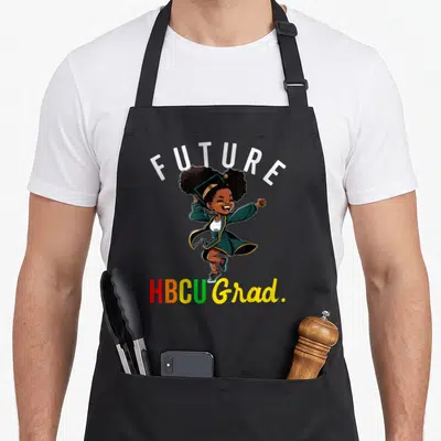 Future love grade apron - Jumping graduate in green gown with FUTURE HBCU Grad text in red orange yellow and green — shown on a black cotton canvas apron against a white background